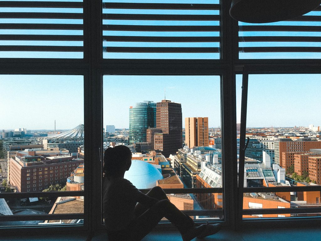 pexels-photo-2516400-2516400 Silhouette of a person sitting by a window overlooking the Berlin cityscape.